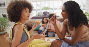 Oturma odasındaki kanepede oturup pizza yiyen çeşitli bayan arkadaşlar. evde kaliteli zaman geçirmek.