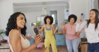 Mutlu çeşitli bayan arkadaşlar oturma odasında mikrofona şarkı söylüyorlar. evde kaliteli zaman geçirmek.
