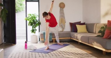 Çift cinsiyetli olmayan beyaz kadın yoga yapıyor, esneme hareketleri yapıyor. Evde yalnız geçirilen kaliteli zaman, bedensel kapsama..