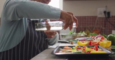 Asyalı son sınıf öğrencisi kadın evdeki mutfakta sebze salatasının üzerine zeytin yağı döküyor. emeklilik yaşam tarzı ve yaşam konsepti