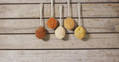 Tahta yüzeyde çeşitli baharatlarla duran kaşıkların videosu. yemek, baharatlar, baharatlar, tat ve lezzet kavramı.