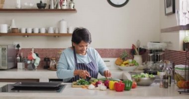 Asyalı son sınıf öğrencisi bir kadın evde mutfakta sebze doğrayan bir önlük giyiyor. emeklilik yaşam tarzı ve yaşam konsepti