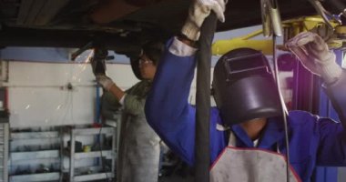 İki farklı kadın araba tamircisinin kaynak yaptığı bir video. Araba tamirhanesinde çalışmak ve küçük kadınsı iş konsepti yürütmek..