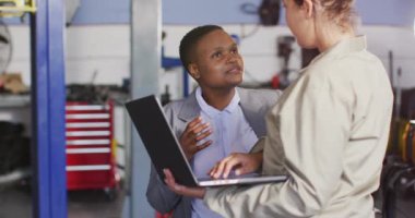 Dizüstü bilgisayarlı iki farklı araba tamircisi ve işyeri sahibinin araba parçaları arama videosu. Araba tamirhanesinde çalışmak ve küçük kadınsı iş konsepti yürütmek..
