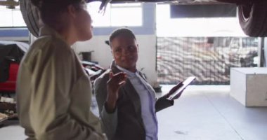 İki farklı kadın araba tamircisi ve tablet kontrol arabalı iş sahibinin videosu. Araba tamirhanesinde çalışmak ve küçük kadınsı iş konsepti yürütmek..