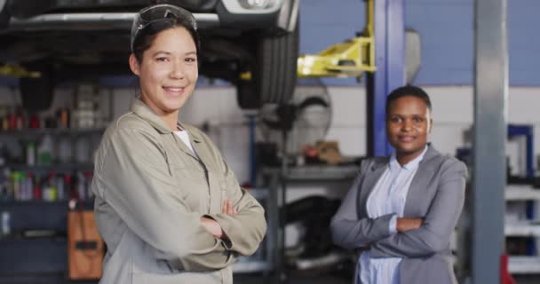 カメラを見て2つの多様な幸せな女性の車の整備士やビジネスオーナーのビデオ 車修理工場で働き女性らしい小さなビジネスコンセプトを運営しています — ストック動画