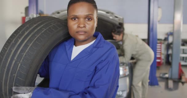 Nagranie Afrykańskiej Amerykańskiej Mechaniki Samochodowej Trzymającej Oponę Praca Warsztacie Samochodowym — Wideo stockowe