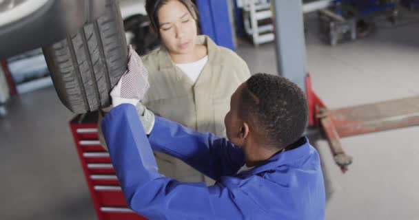 2つの多様な女性の車の整備士の変更タイヤのビデオ 車修理工場で働き女性らしい小さなビジネスコンセプトを運営しています — ストック動画