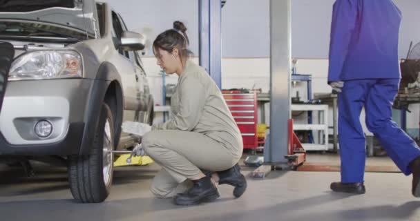 白人女性の車の整備士のビデオタイヤを交換します 車修理工場で働き女性らしい小さなビジネスコンセプトを運営しています — ストック動画