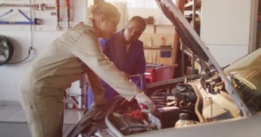 İki farklı kadın araba tamircisinin konuşurken ve araba tamir ederken çekilmiş videosu. Araba tamirhanesinde çalışmak ve küçük kadınsı iş konsepti yürütmek..