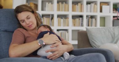 Yeni doğmuş bir bebekle koltukta uyuyan yorgun beyaz annenin videosu. annelik, ebeveyn sevgisi ve yeni doğan bebek konseptiyle ilgilenmek dijital olarak üretilmiş video.