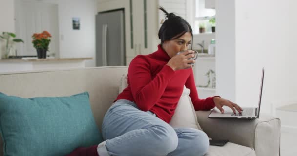 视频中快乐的比利卡妇女头戴头巾坐在沙发上喝咖啡和使用笔记本电脑 生活方式 在家里度过与技术概念相关的闲暇时间 — 图库视频影像
