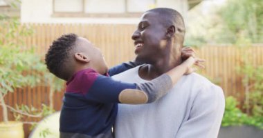 Video of happy african american father and son hugging in garden. Family, spending quality time together at home and garden concept.