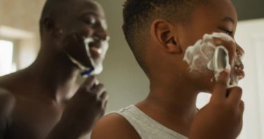 Video of happy african american father and son shaving in bathroom. Family, spending quality time together at home concept.