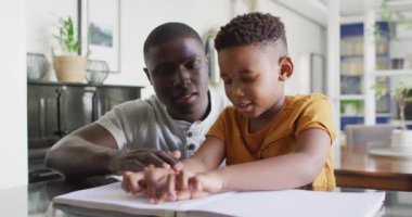 Video of african american father helping blind son reading in braille. Family, spending quality time together at home concept.