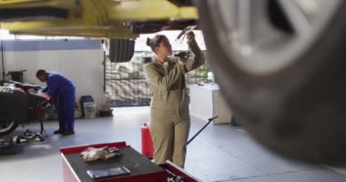 Video of biracial female car mechanic repairing car. Working in car repair shop and running small feminine business concept.
