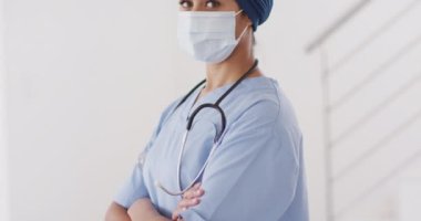 Video of biracial female doctor in hijab and face mask looking at camera. Health, medicine, prevention and covid 19 pandemic concept.