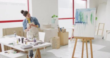 Video of biracial female artist preparing paints and working in studio. Art, crafts, creativity and creation process concept.