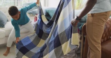 Video of midsection of african american father and son preparing base from chairs and blanket. Family, spending quality time together at home concept.