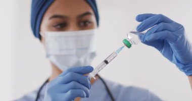 Video of biracial female doctor in face mask with vaccine. Health, medicine, prevention and covid 19 pandemic concept.
