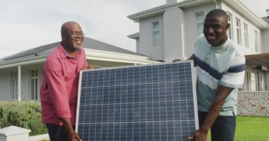 Güneş panelini taşıyan iki Afrikalı Amerikalı adamın videosu. Enerji, enerji ve yakıt teknolojisi ve dijital arayüz konsepti dijital olarak oluşturulmuş video.