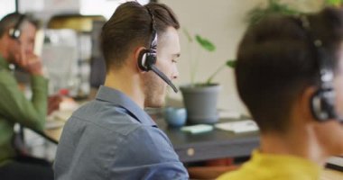 Kafkasyalı mutlu iş adamının portresi telefon kulaklığı takıyor ve ofisteki kameraya bakıyor. Modern bir ofiste çalışıyorum..