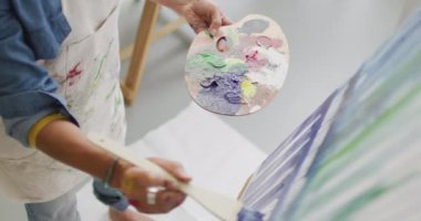 Video of midsection of biracial female artist painting in studio. Art, crafts, creativity and creation process concept.