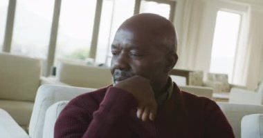 Video of thoughtful senior african american men sitting in living room alone. Retirement lifestyle, spending time alone.