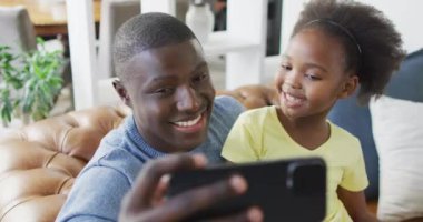 African american father and daughter using smartphone. Enjoying quality family time together at home and using technology.