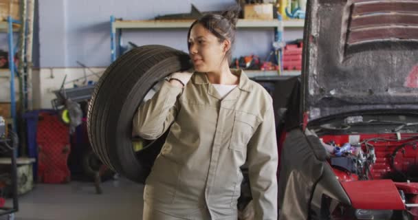 Video Happy Biracial Female Car Mechanic Holding Tyre Working Car — Stock Video