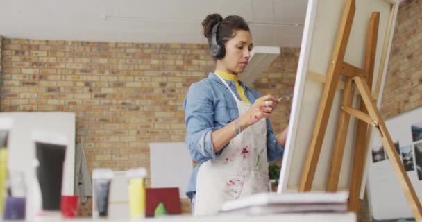 Video Biracial Female Artist Headphones Painting Studio Art Crafts Creativity — Stockvideo