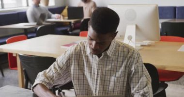 Afro-Amerikalı iş adamı masada oturuyor ve ofiste dizüstü bilgisayar kullanıyor. Modern bir ofiste çalışıyorum..