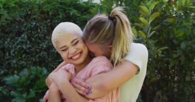 Portrait of happy diverse female couple embracing and smiling in garden. Domestic lifestyle, spending free time at home.