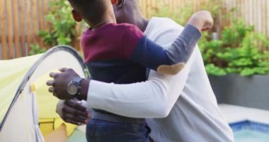 Video of happy african american father and son hugging in garden. Family, spending quality time together at home and garden concept.