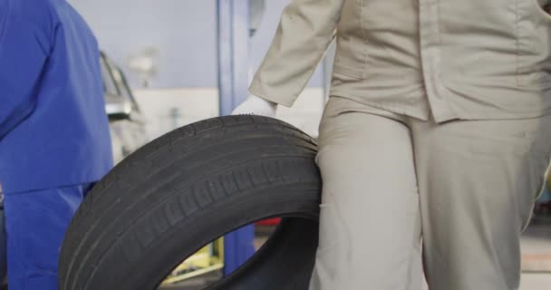 Video Midsection Biracial Female Car Mechanic Holding Tyre Working Car — Stockvideo