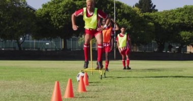 Video of diverse group of male football players warming up on field, running and kicking ball. Male football team, inclusivity and fitness in team sports.