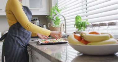 Video of midsection of african american woman preparing meal in kitchen. Lifestyle, cooking, household and spending time at home concept.