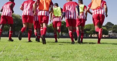 Video of diverse group of male football players warming up on field, running. Male football team, inclusivity and fitness in team sports.