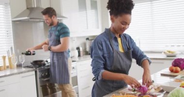 Video of happy diverse couple preparing meal, cutting vegetables in kitchen. Love, relationship and spending quality time together at home.