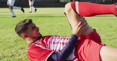 Video of biracial football player on field lying fouled. Male football team, inclusivity and fitness in team sports.