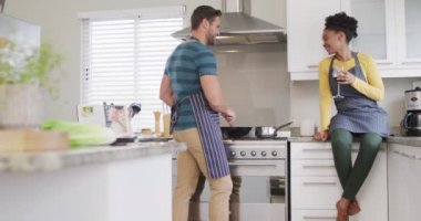 Video of happy diverse couple preparing meal, drinking wine and having fun in kitchen. Love, relationship and spending quality time together at home.