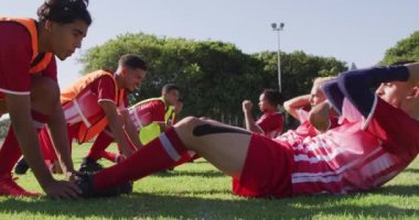 Video of diverse group of male football players warming up on field, doing sit-ups. Male football team, inclusivity and fitness in team sports.