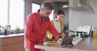 Birlikte yemek pişiren, sebze doğrayan ve mutfakta tablet kullanan mutlu çift. Evde kaliteli zaman geçirmek.