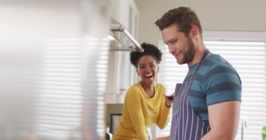 Video of happy diverse couple preparing meal, drinking wine and having fun in kitchen. Love, relationship and spending quality time together at home.