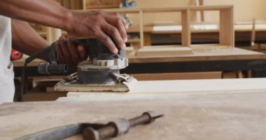 Close up of african american male carpenter hand's using an electric grinder to grind wooden plank. Carpentry, craftsmanship and handwork concept