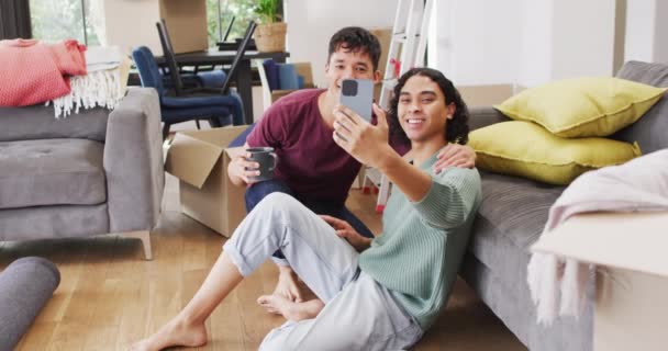 Happy Diverse Male Couple Moving House Drinking Coffee Taking Selfie — Vídeo de Stock