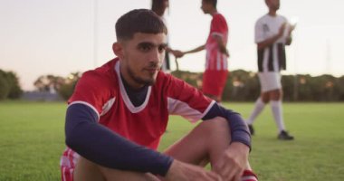 Video of mad biracial football player siting on field. Male football team, inclusivity and fitness in team sports.