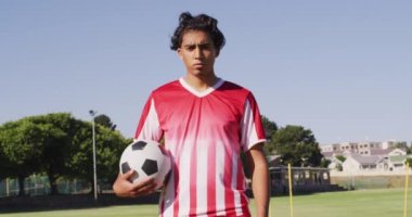 Video of diverse male biracial football player standing on field with ball. Male football team, inclusivity and fitness in team sports.