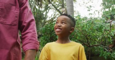 Mutlu kıdemli Afrikalı Amerikalı adam ve torunu bahçede birlikte yürüyorlar. Dışarıda vakit geçirmek, bahçede çalışmak..