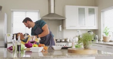 Video of happy diverse couple dancing in kitchen in aprons. Love, relationship and spending quality time together at home.